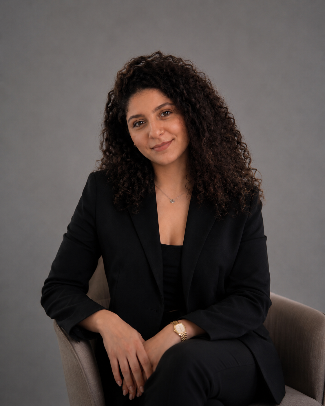 Woman in a black suit sitting on a chair against a gray background